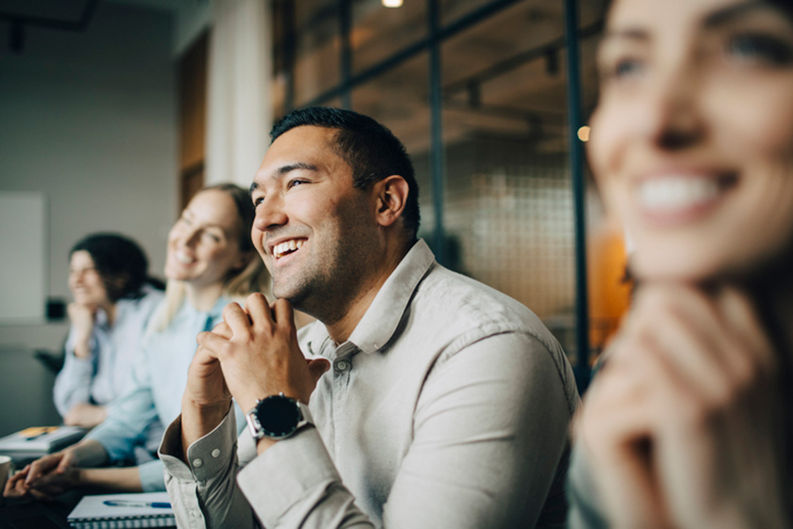 Smiling professionals attentively listening during a meeting or training session in a modern office.